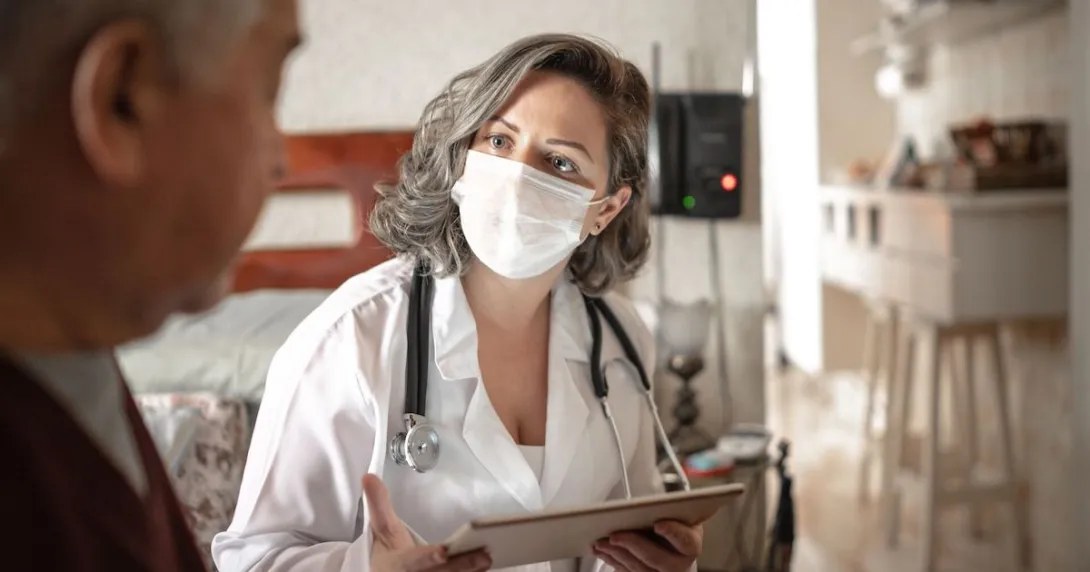 A doctor holding a digital tablet consulting with a senior patient during home visit.