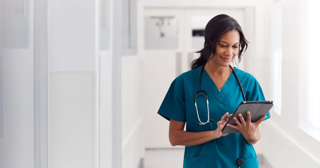 A doctor in scrubs checking a patient's file on a digital tablet