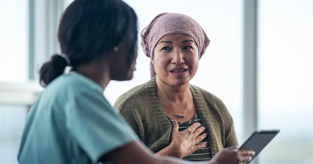 A patient in a headwrap consulting with a doctor who is holding a digital tablet