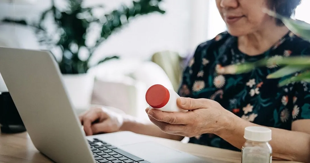 Person sits at table with a laptop while holding a pill bottle