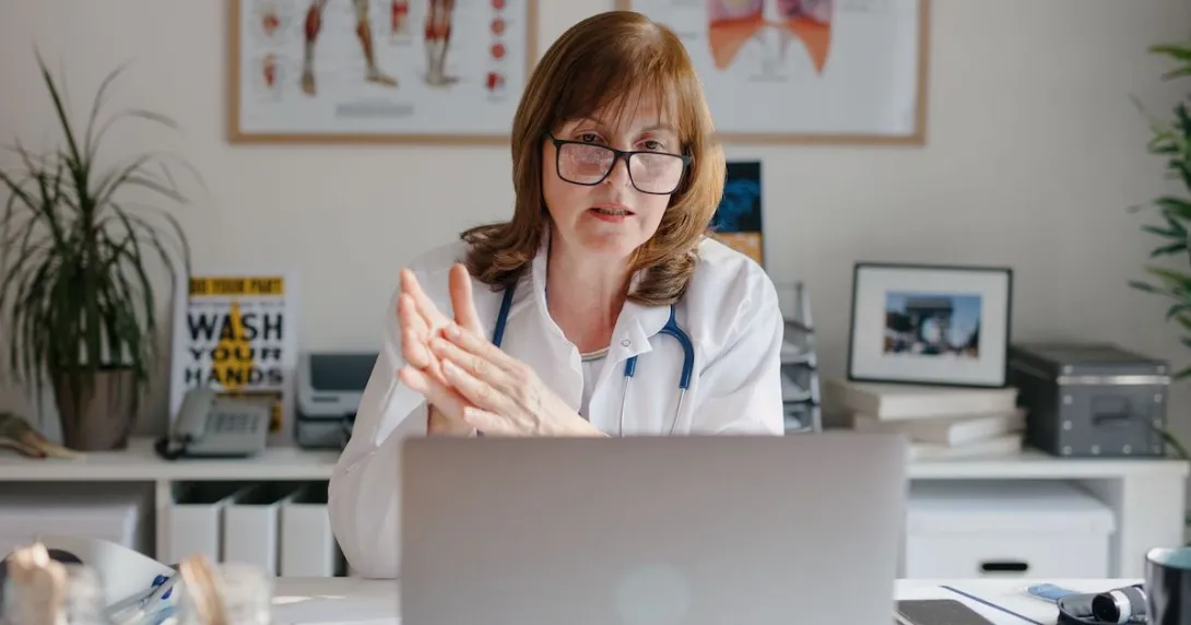 A doctor using a laptop is in an online video consultation with a patient