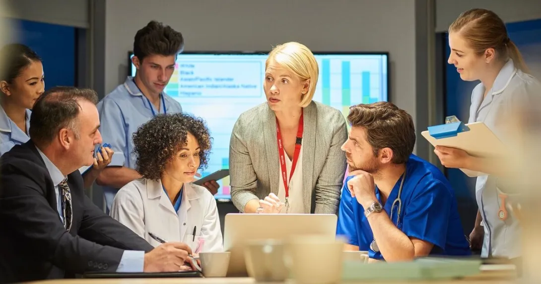 A group of healthcare professionals are meeting in front of a laptop to discuss cybersecurity.