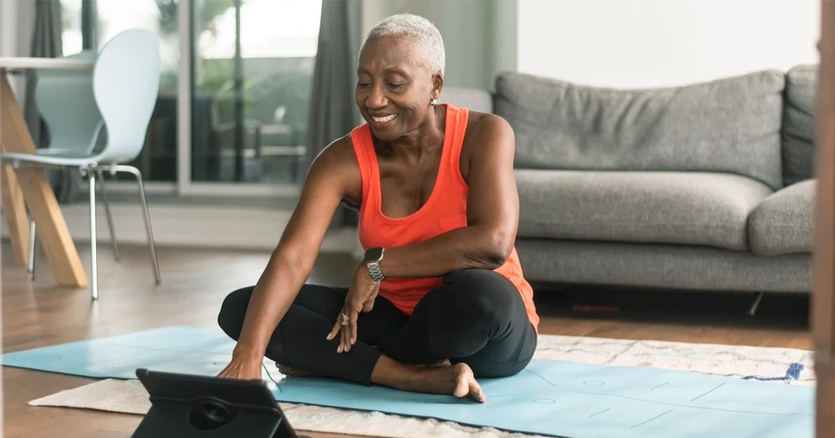 Woman sits on yoga mat in living room looking through data on her tablet Woman sits on yoga mat in living room looking through data on her tablet