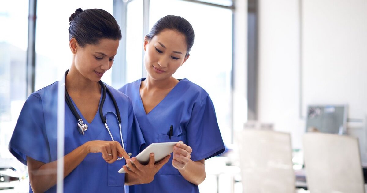 Two nurses checking a patient's medical record on a digital tablet